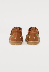 Chaussures en cuir brun avec une sangle Velcro, ornées de motifs brodés colorés de légumes et d'insectes sur les côtés.