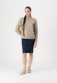 Beige stickad tröja med hög krage, kombinerad med en mörk denimkjol i blyertsstil och ljuskrämfärgade platta skor med ankelremmar.