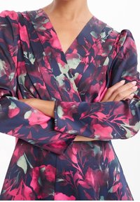 Dlouhý rukáv šaty z námořnické látky s živým květinovým vzorem v růžových a zelených odstínech. Výrazné nabírané ramena a výstřih do V.