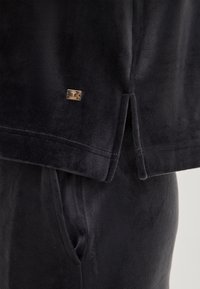 Fleece lounge set in donkergrijs, met een gladde textuur, zijsplitsingen en een rechthoekig metallic logo op de bovenkant.