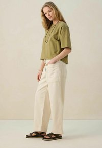 T-shirt cropped vert olive, pantalon large crème avec poches, et sandales noires à lanières croisées. Finitions soignées, coupe décontractée.