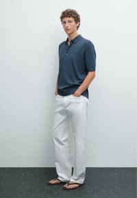 Marineblå polo-shirt med korte ærmer, to knapper ved kraven, parret med hvide bukser, båret med sorte klipklapper, glat stof og afslappet pasform.