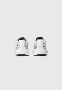 Des chaussures de sport avec une tige en maille blanche et des accents noirs, présentant un talon texturé, des lignes courbées et une semelle rembourrée.