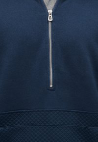 Μπλε του ναυτικού φούτερ με φερμουάρ στο ένα τέταρτο μπροστά, που διαθέτει υφασμένη κάτω επιφάνεια με διαμάντι μοτίβο και λείο ύφασμα στο πάνω μέρος.