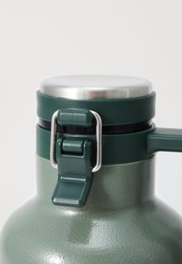 Green insulated water bottle with a textured finish, stainless steel lid, and a secure clamp closure. Features a sturdy handle for easy use.