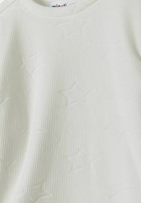 Haut en coton crème avec texture côtelée et motif étoilé en relief. Design col rond, tissu doux, sans matériel ni accents visibles.