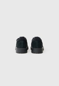 Sapatos de camurça pretos com um upper texturizado e uma sola de borracha preta sólida, apresentando uma forma arredondada e sem logótipos ou enfeites visíveis.