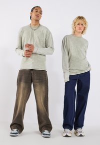 Langermede lysegrønne skjorter med falmet tekstur, parret med brune og mørkeblå løse jeans. Sko med varierte farge mønstre.