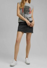 Grijze graphic T-shirt met korte mouwen en abstracte print, gecombineerd met een zwarte denimrok met rafelige zoom en subtiele slijtage. Witte sneakers.