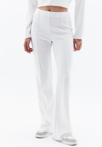 Witte uitlopende broek gemaakt van zachte, gestructureerde stof met verticale naden. Gecombineerd met grijze en witte sneakers, met een aansluitende taille.