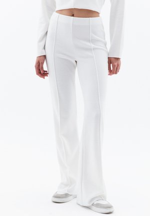 Witte uitlopende broek gemaakt van zachte, gestructureerde stof met verticale naden. Gecombineerd met grijze en witte sneakers, met een aansluitende taille.