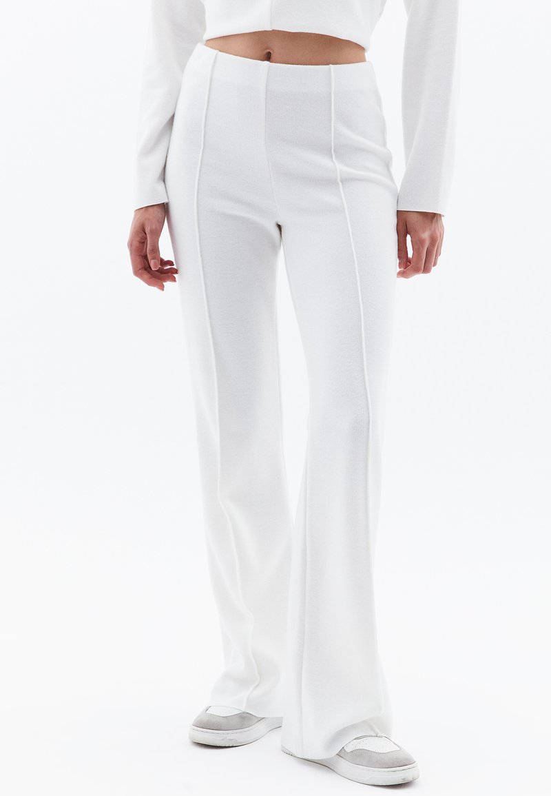 Witte uitlopende broek gemaakt van zachte, gestructureerde stof met verticale naden. Gecombineerd met grijze en witte sneakers, met een aansluitende taille.
