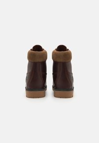 Stivaletti ankle in pelle marrone con risvolto in suede beige, punta arrotondata e suola in gomma resistente con un leggero motivo di battistrada.