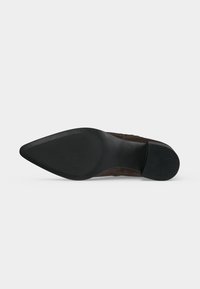 Vue de la semelle d’une chaussure en cuir marron à bout pointu avec une semelle en caoutchouc noir texturé à l’avant et un talon noir solide.