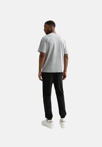 Grijs T-shirt met korte mouwen en zwarte joggingsbroek, gecombineerd met witte sneakers. Eenvoudig ontwerp, zachte textuur, ontspannen pasvorm, minimale details.