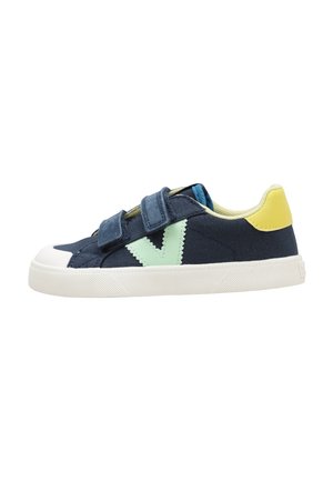 Zapatilla azul marino con suela blanca, logo lateral verde menta, parche amarillo en el talón y dos tiras azul marino de velcro.