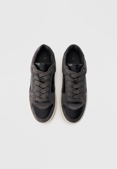 Σκούρα γκρι αθλητικά παπούτσια με μίγμα σουέτ και δερμάτινων υλικών. Στρογγυλερή μύτη, λεπτομέρειες με τρύπες και επίπεδα κορδόνια. Λευκή ελαστική σόλα.