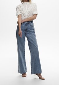 Vit broderie anglaise-blus med volangkrage, i kombination med ljusblå högmidjade vida jeans. Klara klacksandaler.