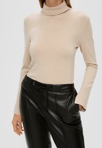 Beige Rollkragenpullover mit langen Ärmeln, aus weichem Stoff gefertigt, kombiniert mit schwarzen Lederhosen mit Kordelzug und Seitentaschen.