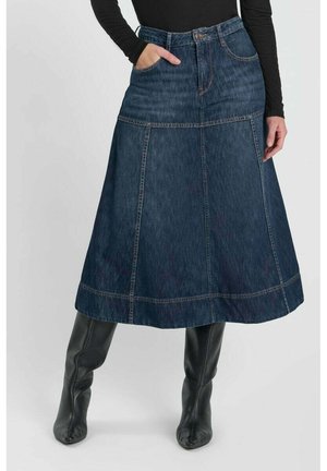 Donna che indossa una gonna a trapezio in denim blu scuro con tasche anteriori e stivali neri al ginocchio, vestita con una maglia nera a maniche lunghe.
