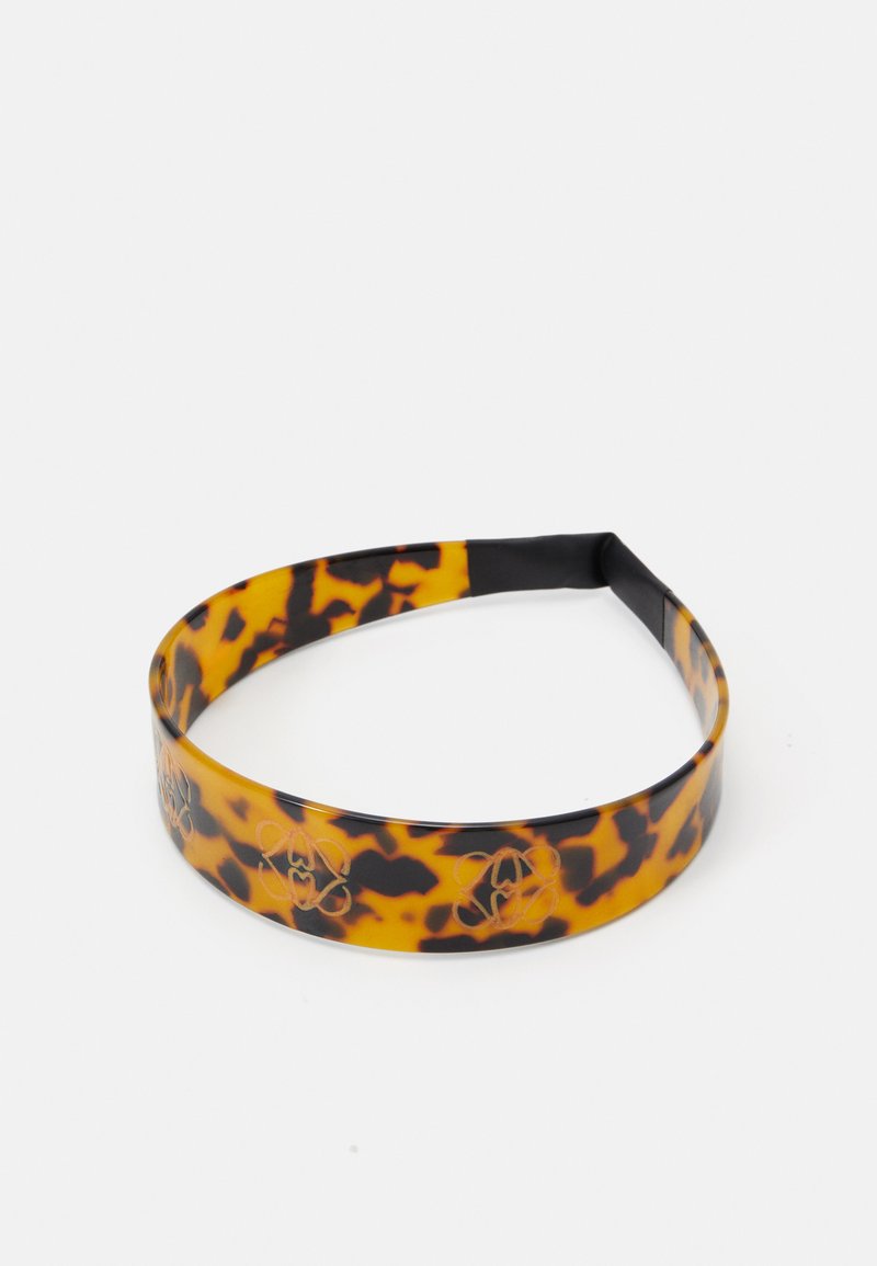 Un bandeau en écaille de tortue en plastique brillant, présentant un motif noir et orange avec des accents floraux gravés autour du bandeau.