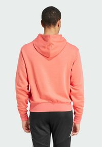 Koraalkleurige hoodie met een trekkoord capuchon, ribgebreide manchetten en onderrand, en een gladde textuur, gecombineerd met zwarte sportbroeken.