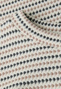 Gros plan sur un tissu tricoté avec des rangées répétées de petits motifs en forme de cœur beige et noir sur un fond crème.