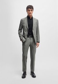 Gray checked suit with a tailored fit, paired with a black button-up shirt. Features a structured lapel and black leather shoes.