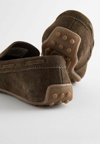 Braune Wildleder-Slipper mit einer strukturierten Gummisohle, die kleine Rutschpunkte aufweist, sowie genähten Details entlang der Kanten.