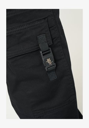 Pantaloni cargo neri con finitura testurizzata, dotati di una tasca laterale chiusa da una fibbia nera e un piccolo dettaglio del logo dorato.