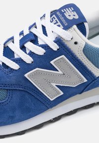 Blå mocka och mesh sneakers har en stor grå "N"-logotyp, vita snören och en ljusgrå mellansula med texturerad detaljering.