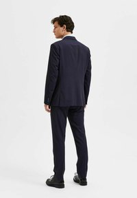 Marinblå kostym med skräddarsydd design, slätt tyg och tvåknäppning. Byxorna är slim fit med en subtil lyster. Svarta dress skor.