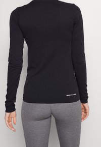 Top atletico nero a maniche lunghe con superficie testurizzata, caratterizzato dal logo Dri-FIT all'orlo, abbinato a leggings grigi aderenti.