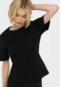 Sort T-shirt med korte ærmer og rund hals. Har en tætsiddende pasform og diskrete syninger, lavet af blødt, strækbart stof.