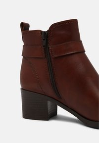 Hnědé kožené kotníkové boty s bo�čním zipem, šitými detaily a krátkým blokovým podpatkem. Hladký povrch s lesklým finish.