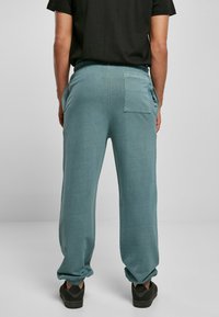 Lys blå joggebukser laget av et glatt stoff, med elastisk midjebånd, sidelommer og en enkelt baklomme.