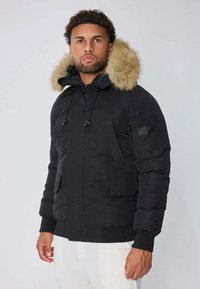 Veste doudoune noire avec une capuche doublée de fourrure, dotée de poches avant, de poignets élastiques et d'une fermeture éclair. Texture lisse, design chaud.