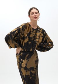 Lange mouwen, cropped top van satijnen stof met een zwart-gouden tie-dye patroon; een strakke rok die de top aanvult. Grote hoepeloorbellen.
