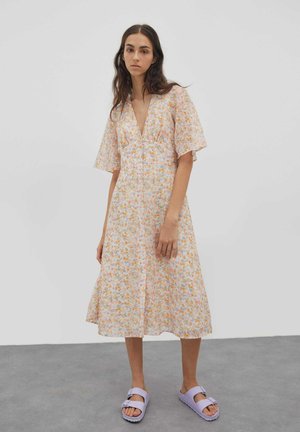 Robe midi florale dans des couleurs pastel claires avec des manches courtes en volants, un décolleté en V et un avant à boutons. Assortie avec des sandales lavande.