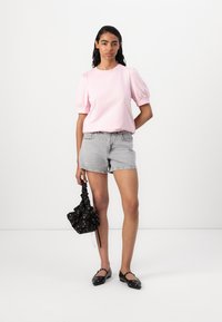 Rosa kortärmad topp med puffärmar, tillsammans med ljusgrå denimshorts. En svart blommönstrad väska och svarta platta skor fulländar looken.
