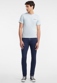 Tricou din bumbac de culoare albastru deschis, cu mâneci scurte și guler rotund, combinat cu blugi skinny negri și adidași alb-negru. Detaliu cu logo pe tricou.
