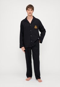 Set de pijamale negre format dintr-o cămașă cu nasturi, cu mâneci lungi și un buzunar pe piept, completată de pantaloni lejeri asortați.