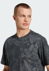 Mørkegrå trenings t-skjorte med en teksturert overflate, rund hals, korte ermer og subtilt grafisk trykk, med en liten logo på brystet.