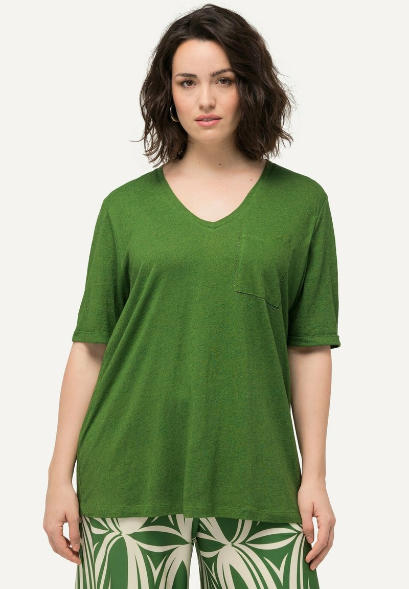 Camiseta verde de manga corta con cuello en V, con bolsillo en la parte delantera y puños enrollados, hecha de una suave tela texturizada. Combinada con pantalones estampados.