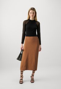 Zwarte lange mouwen top met transparante mouwen, bruin gebreid rok tot halverwege de dij, zwarte sandalen met bandjes en een gestreepte handtas.