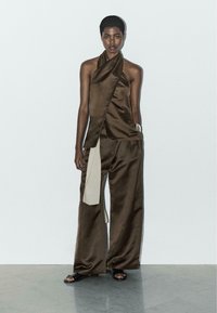 Bruine satijnen haltertop gecombineerd met wijde broek, met een contrasterend beige zijpaneel. Soepele textuur, minimalistisch design en een ontspannen pasvorm.