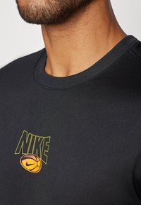 Svart atletisk T-skjorte med rund hals. Forsiden har et flerfarget Nike-logo med et basketballgrafikk. Glatt tekstur.