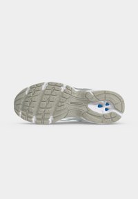 Σόλα αθλητικού παπουτσιού New Balance που δείχνει υφασμένο γκρι καουτσούκ με μπλε λεπτομέρειες και το όνομα της μάρκας στο κέντρο.
