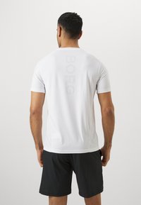Weißes, kurzärmeliges Sportshirt mit einem vertikalen "BORG"-Druck auf dem Rücken. Glatte Textur; kombiniert mit schwarzen Shorts.