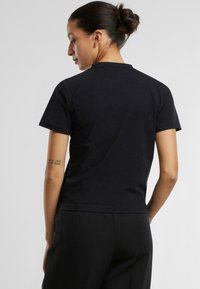 Černé bavlněn�é tričko s kulatým výstřihem, krátkými rukávy a přiléhavým střihem. Má hladkou texturu a minimalistický styl.